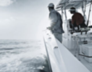 Two anglers standing at the rail of a boat fishing on choppy open water.