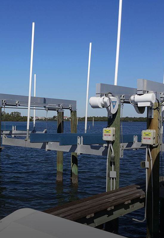 Boat lift with white guide posts and control boxes at a waterfront dock over calm water.