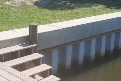 Concrete seawall with wooden dock steps and pilings along a waterway.