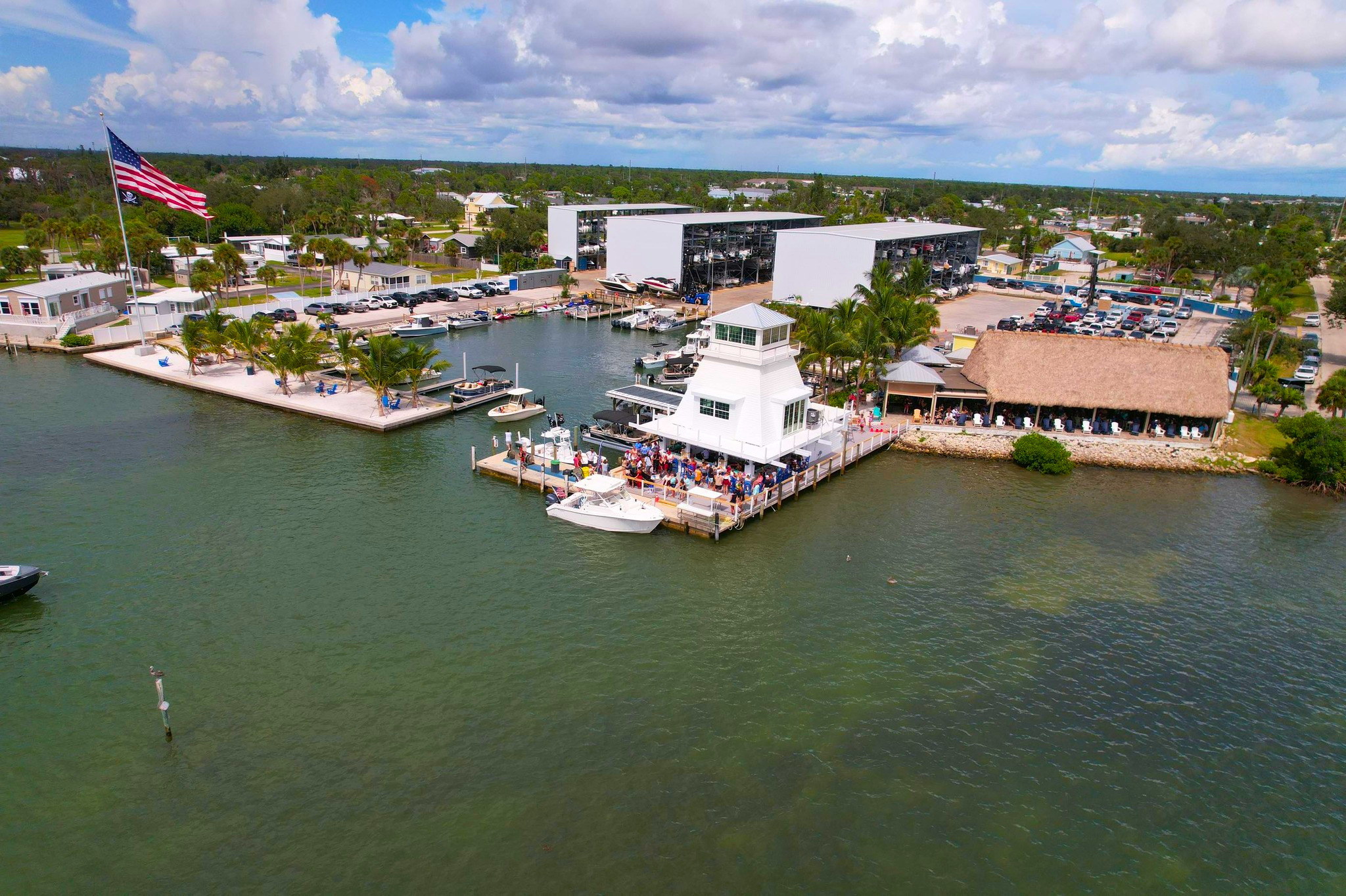 Aerial view of a marina with dry-stack boat storage buildings, docked boats, and a thatched-roof waterfront bar at an unnamed marina, Florida.