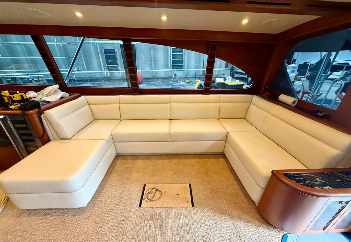 Newly upholstered cream U-shaped saloon seating with mahogany trim inside a motor yacht, with tools and materials visible in the background.