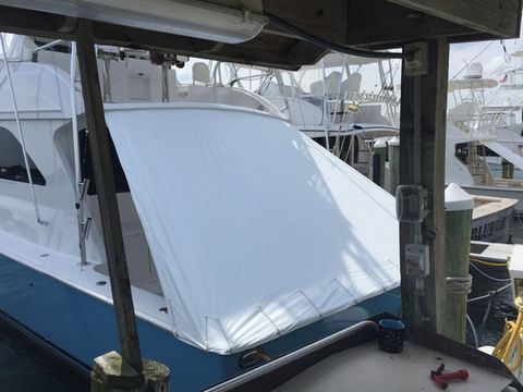 White canvas cover fitted over the stern of a blue-hulled sport fishing boat in a dock slip.