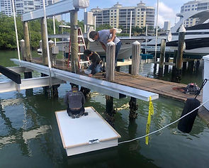 Two workers installing a dock lift and dock section at a marina with yachts moored nearby.