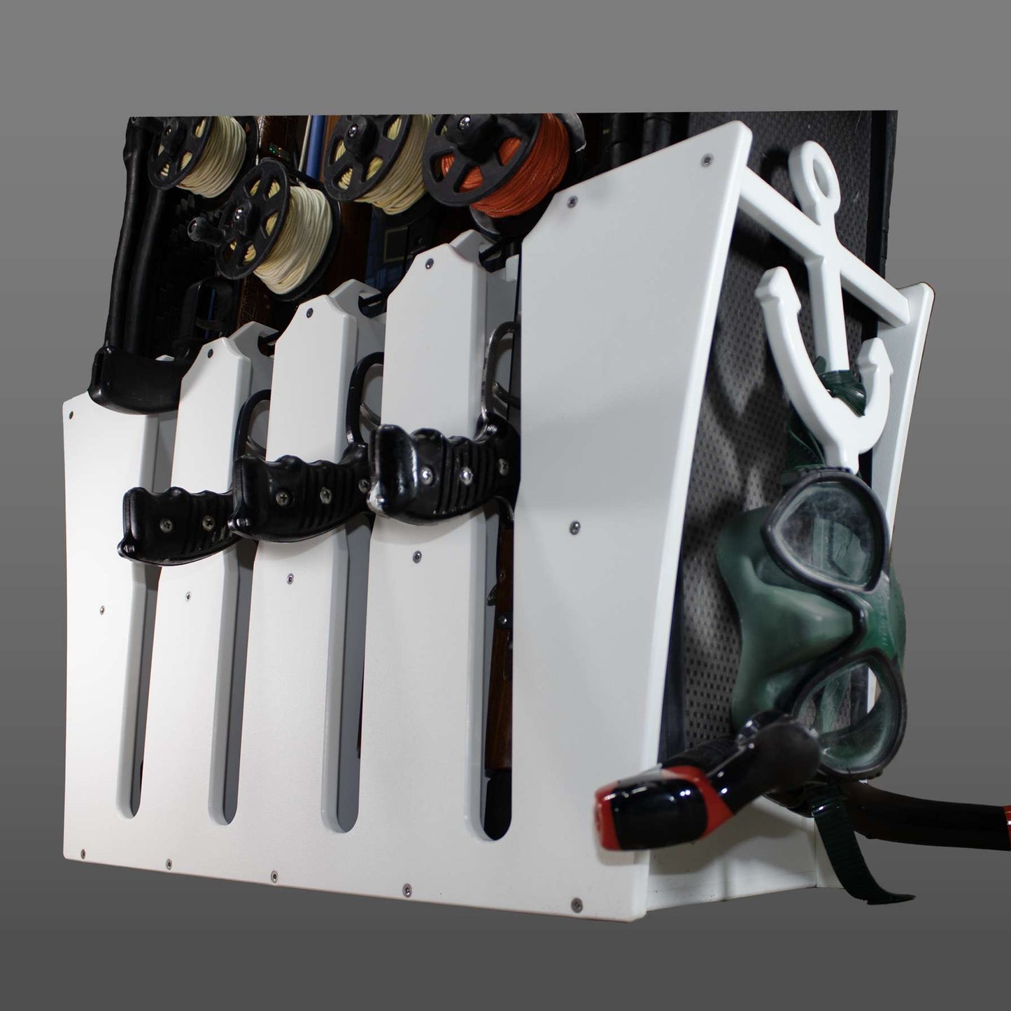 White wall-mounted dive gear rack holding dive knives, a mask and snorkel, and line reels, with no business name or town shown.