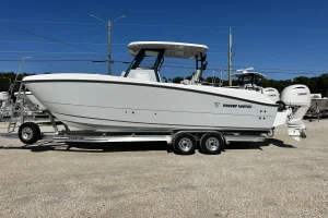 White center-console fishing boat with a T-top on a dual-axle trailer at a boat dealer lot.