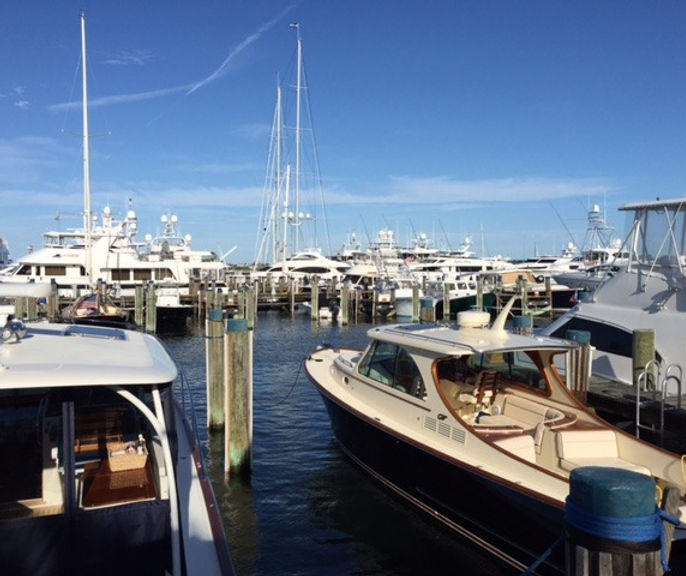 Yachts and a wood-trimmed runabout docked in a busy marina on a clear day, with no specific business name visible.