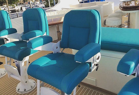 Teal upholstered helm and deck chairs with white pedestal bases on a yacht's teak deck, with marina boats visible in the background.