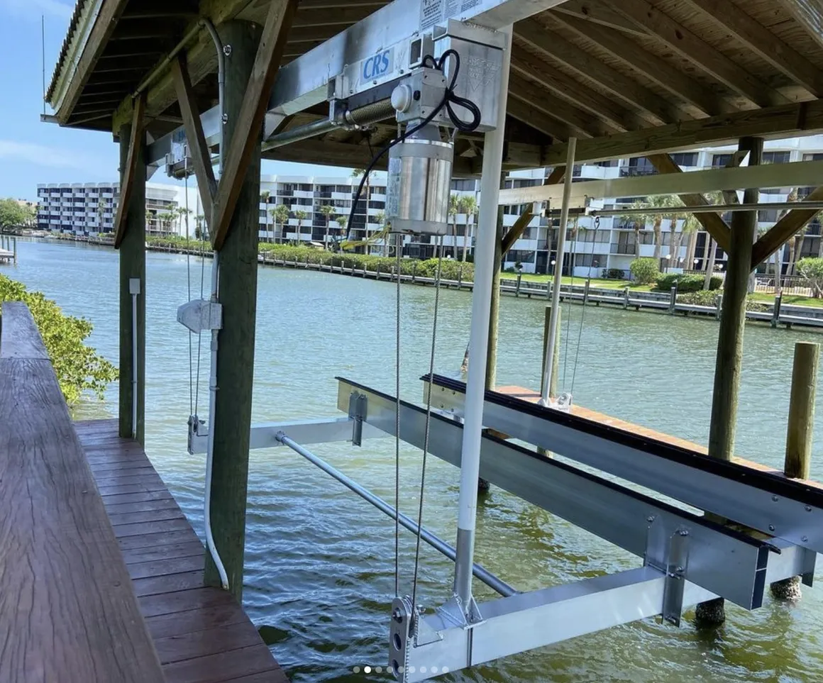 Aluminum boat lift with a CRS motor and cradle under a covered dock on a waterway lined with condominiums.