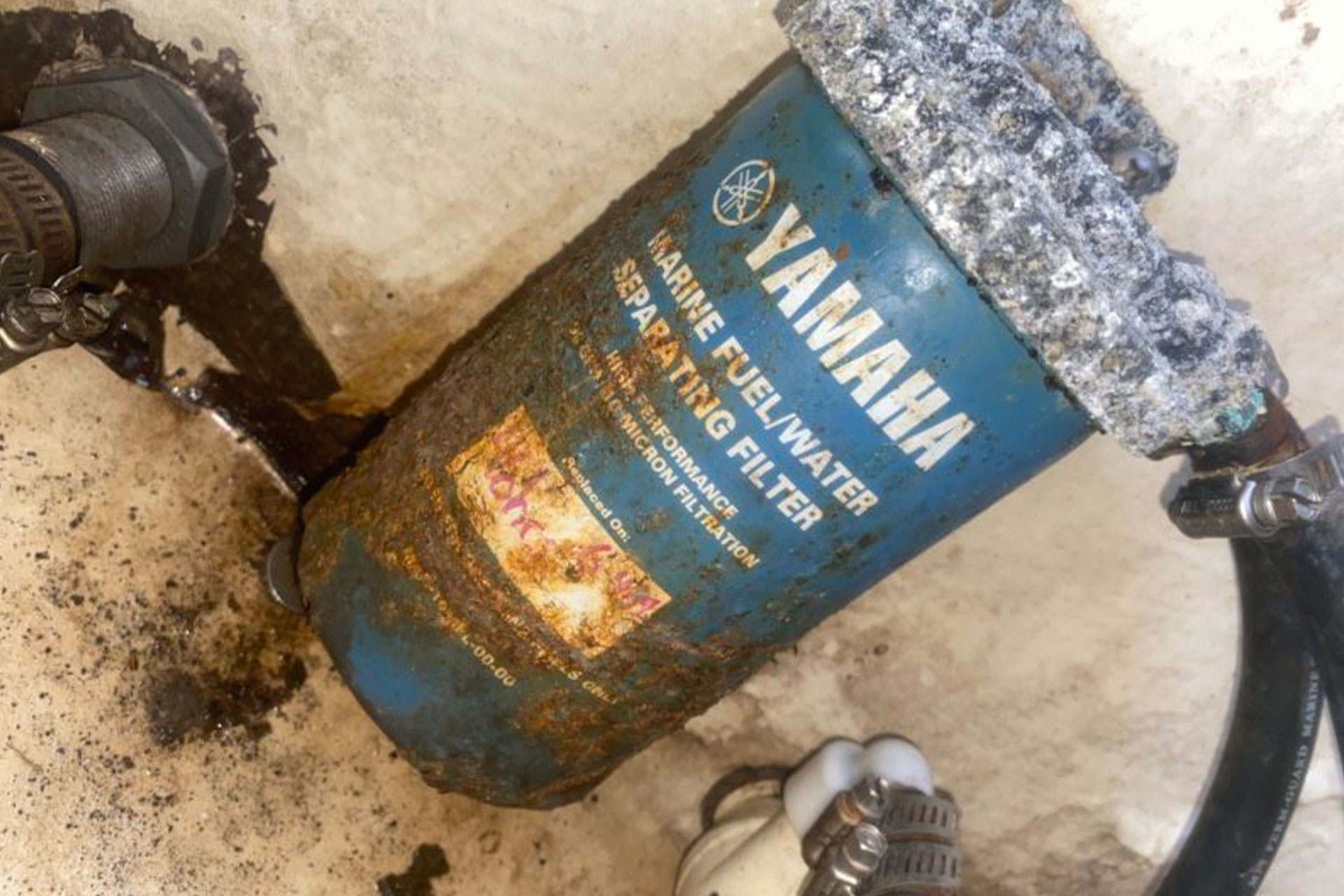 Corroded Yamaha marine fuel/water separating filter leaking fuel onto a deck, with its hose fittings visible.