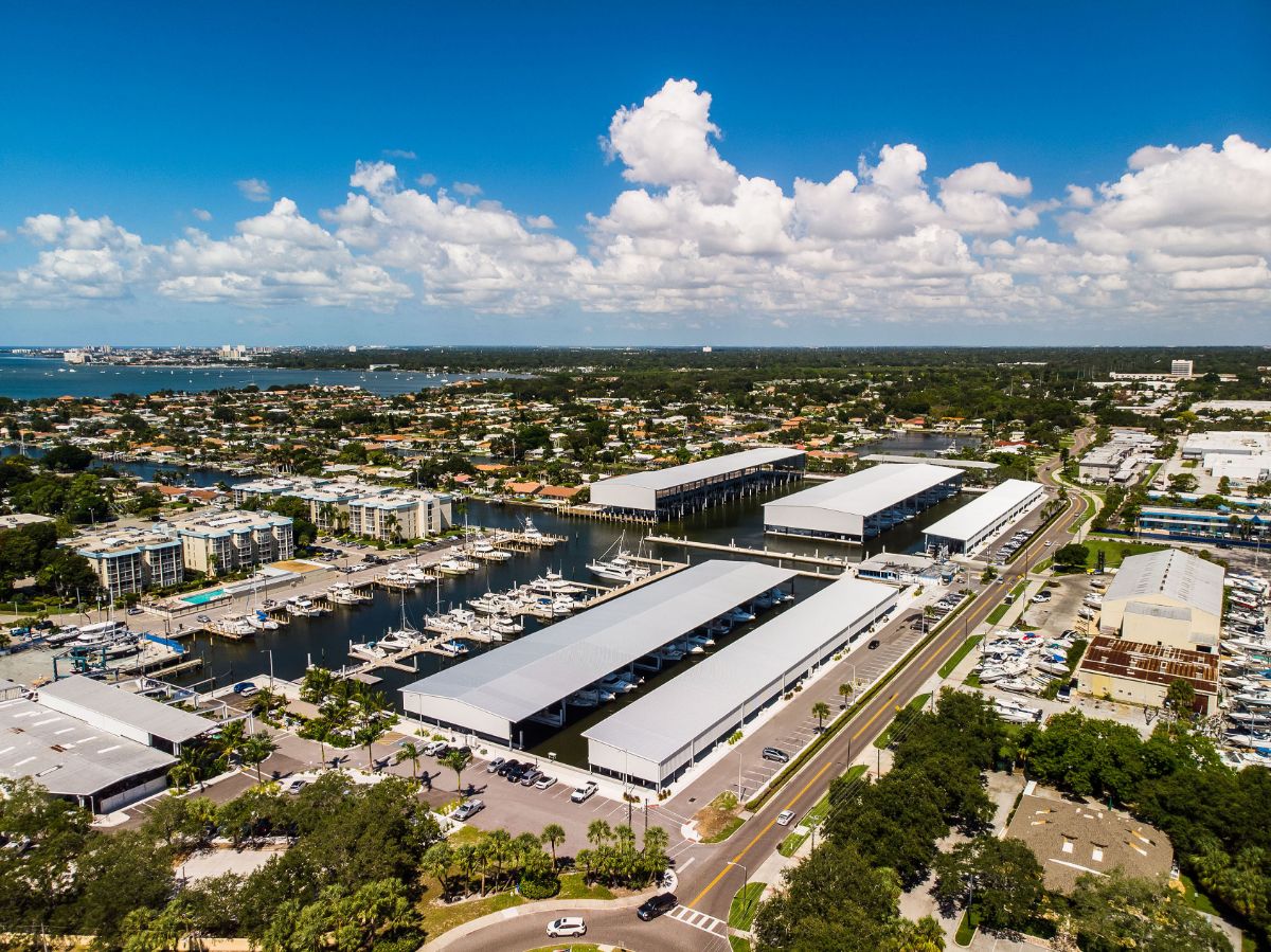 Aerial view of covered boat storage buildings and docked boats at a marina on a canal, with a bay visible in the distance.