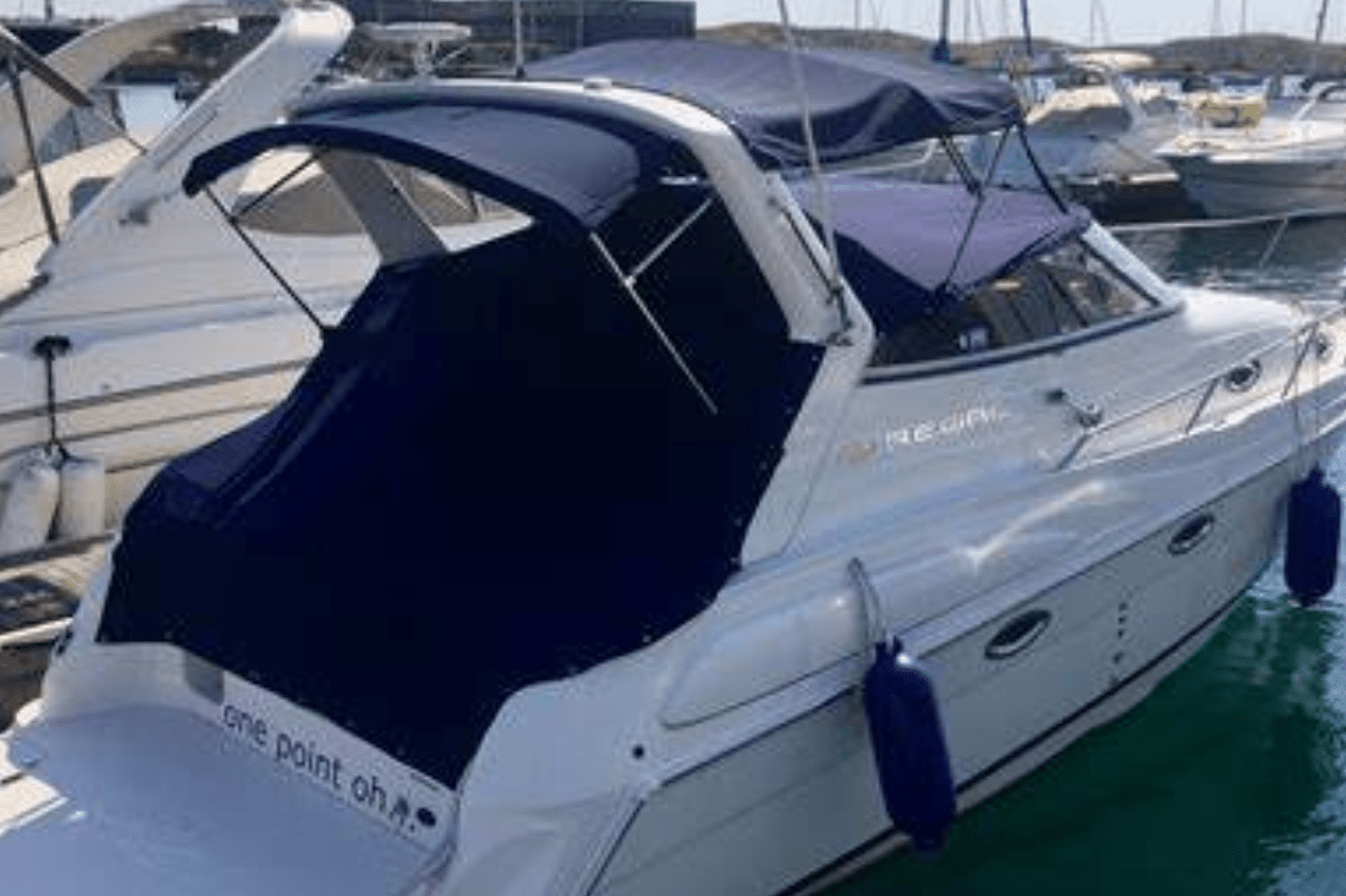 Cruiser motor yacht named Regina with navy blue canvas enclosure and bimini top, moored at a marina dock.