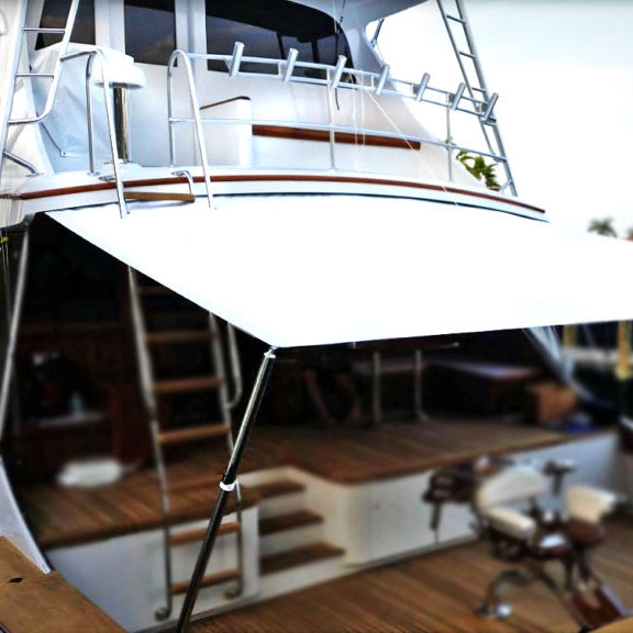 White canvas sunshade stretched over the teak aft deck of a motor yacht, with a helm chair and boarding ladder visible.