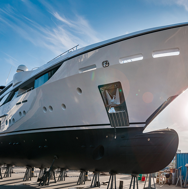 Large white motor yacht with a black hull resting on support stands in a boatyard during refit.
