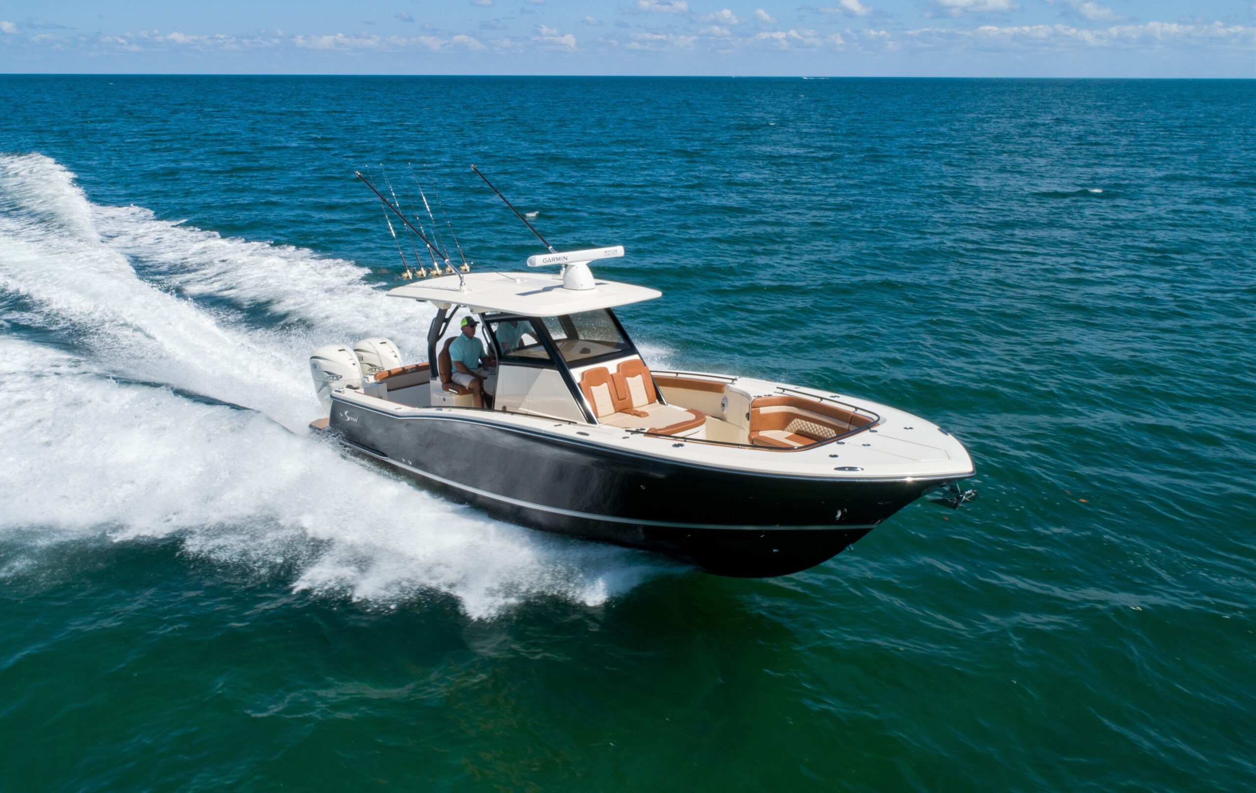 Black-hulled center console sportfishing boat with outboard motors and rod holders running at speed across open ocean water.