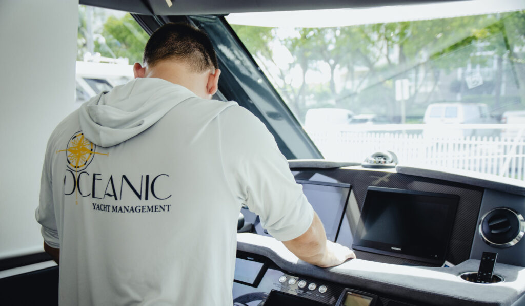 Crew member wiping down the helm console of a yacht at Oceanic Yacht Management, town not shown.
