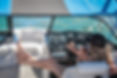 Blurred view from inside a boat's helm looking through the windshield at the dashboard and open water.