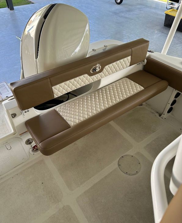 Brown and cream diamond-quilted bench seat with a logo on the backrest, beside an outboard motor cowling, on a boat deck.