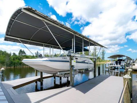 White motorboat resting in a covered boat lift at a dock on a calm waterway, with a second boat moored further along.
