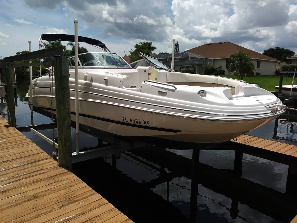 White deck boat with a bimini top resting on a dock lift beside a canal in a Florida residential neighborhood.