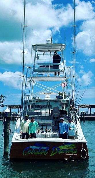 Sportfishing boat Coastal Dreams with a crew of four posing on deck at its dock, with a Garmin electronics mast and rigged fishing rods visible.