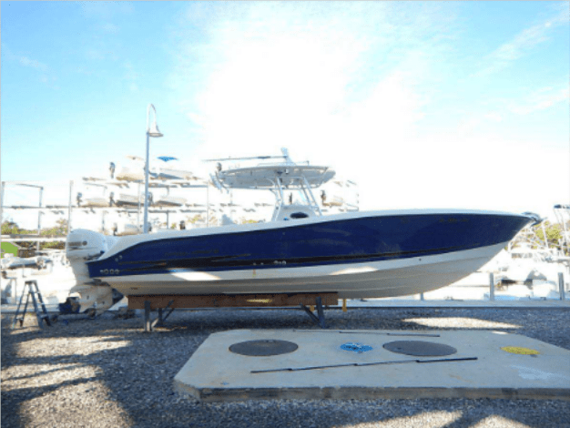 Blue and white center console fishing boat resting on a stand at a dry-stack marine storage yard.