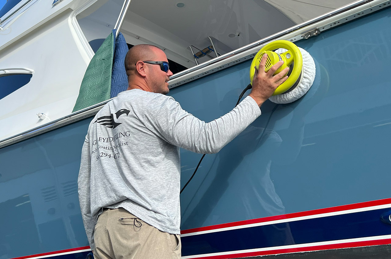 Technician buffing the blue hull of a yacht with a yellow orbital polisher at Eagle Eye Detailing, Jupiter.