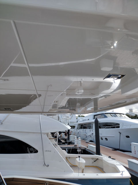 Glossy white fiberglass underside of a flybridge hardtop above a motor yacht moored at a marina dock.