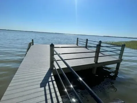Gray composite dock with stainless steel railings extending over calm water under a clear blue sky.