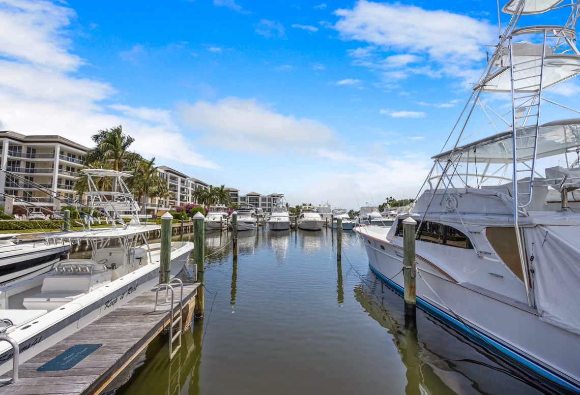Sportfishing and center-console boats moored along a canal-side marina slip with a waterfront condominium complex and palm trees beyond, under a partly cloudy sky.