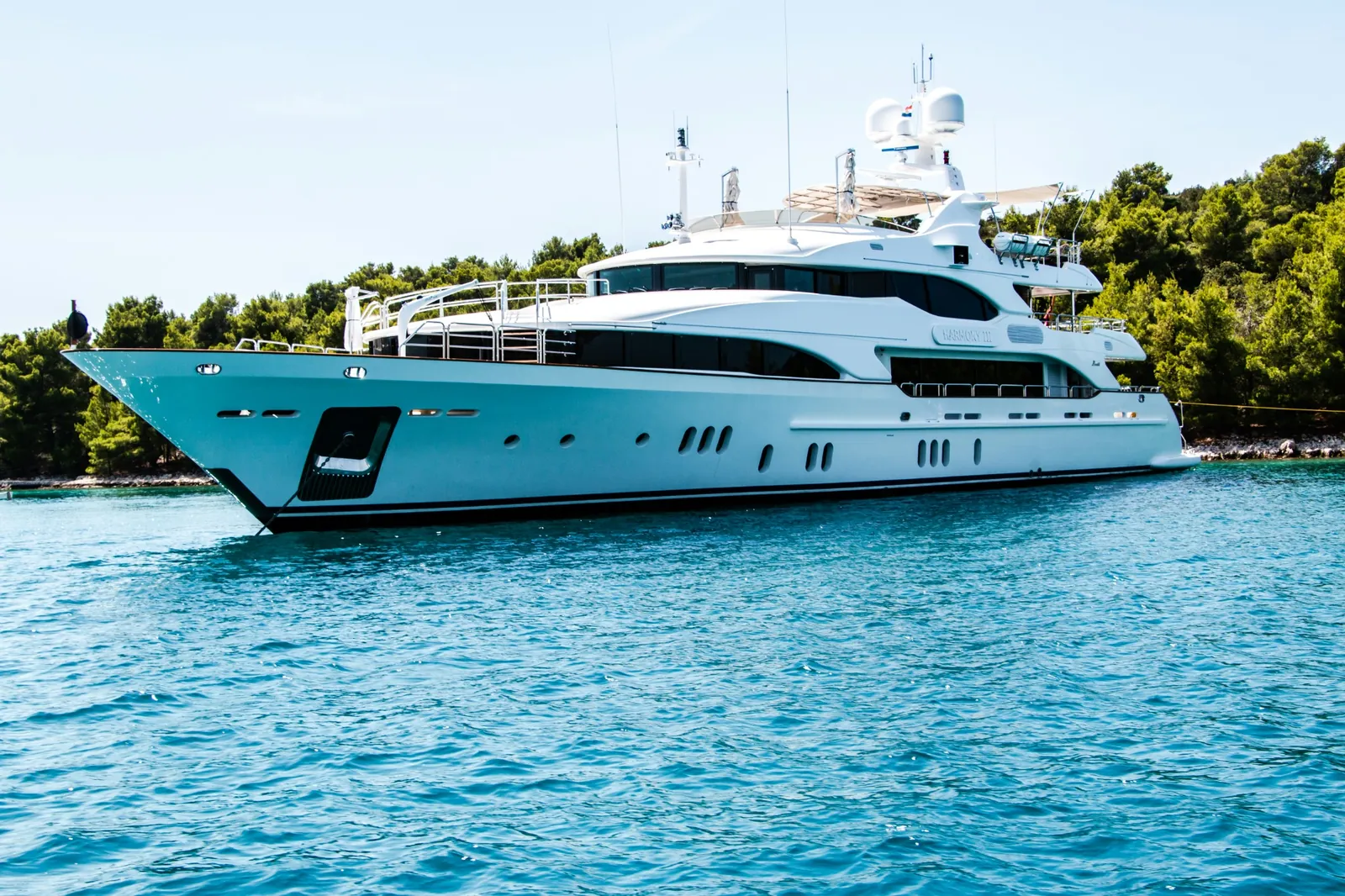 Large white motor yacht named Mastchess at anchor off a pine-lined coast, Croatia.