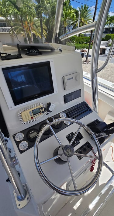 Helm station of a center console boat showing a Simrad chartplotter, VHF radio, engine gauges and a stainless steel steering wheel.