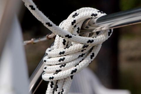 Close-up of a white and black braided rope tied in a knot around a polished stainless steel rail on a sailboat.