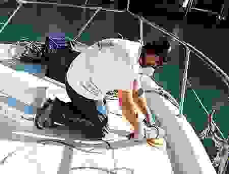 Person in a white cap working on the deck of a sailboat with metal railings and deck hardware visible.