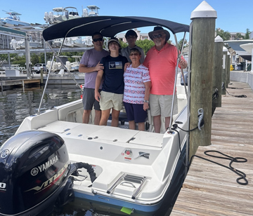 Five people posing on a small Yamaha-powered boat tied up at a marina dock with yachts in the background.