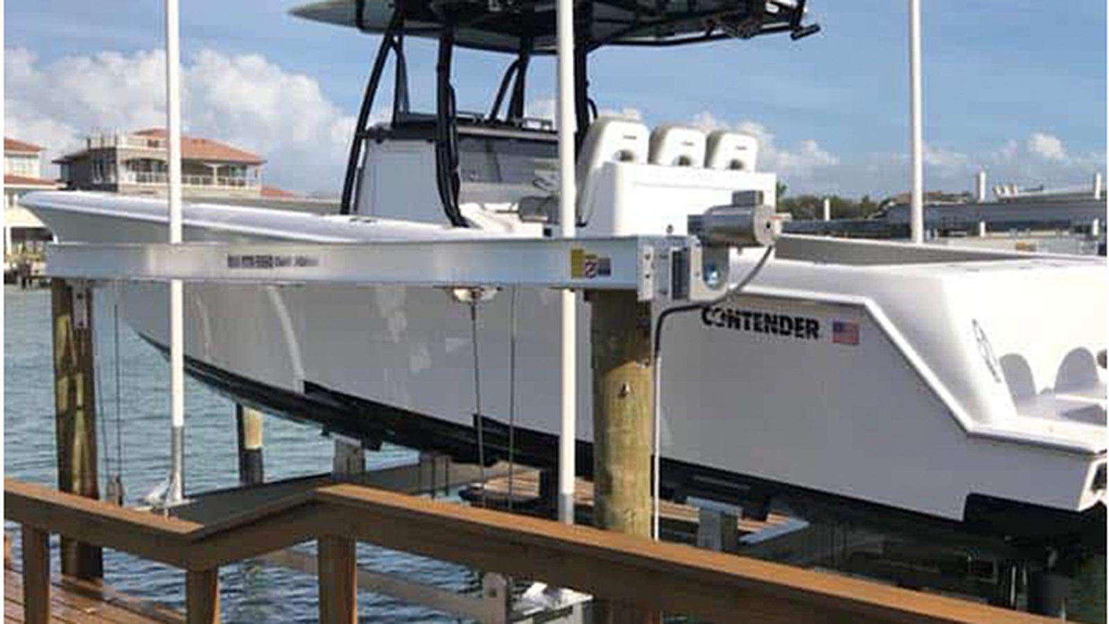 White Contender center console boat raised on a boat lift at a dock, with water and waterfront homes in the background.