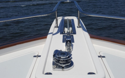 Bow deck of a boat with a stainless steel windlass and railing over open water.