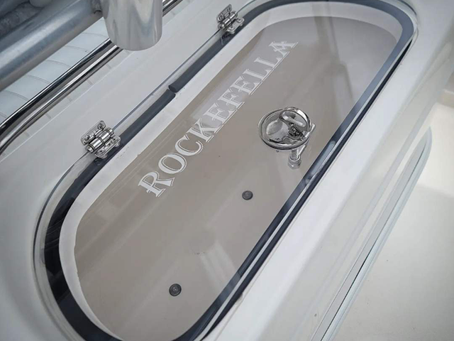 Oval deck hatch with a recessed handle and the name ROCKEFELLA lettered on it, set into the white deck of a boat.