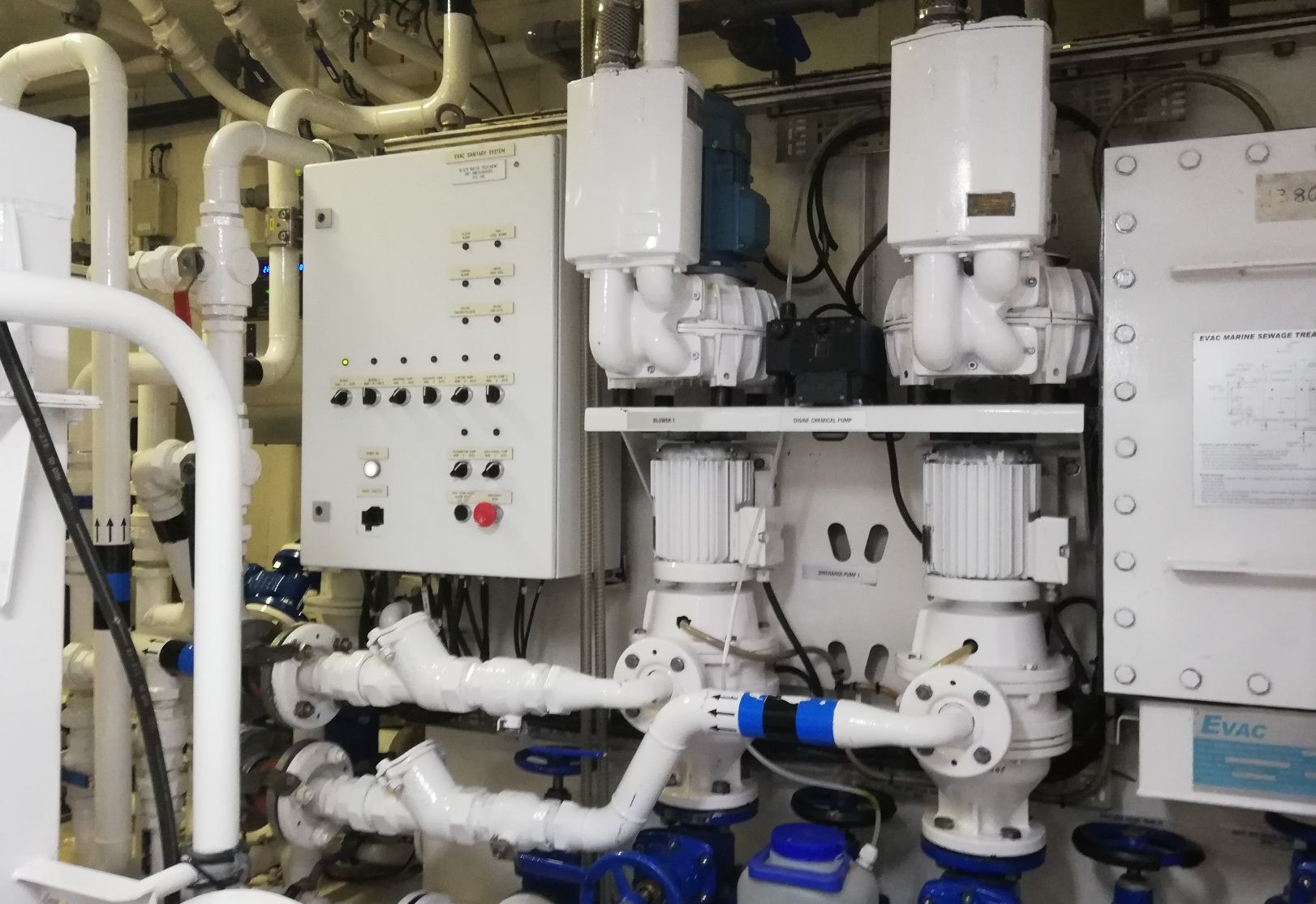Evac marine sewage treatment plant with control panel, blowers, and disinfectant chemical pump in a ship's machinery room.