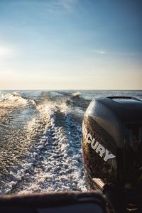 Outboard motor with a Mercury logo on a boat churning a white wake across open water under a hazy sky.