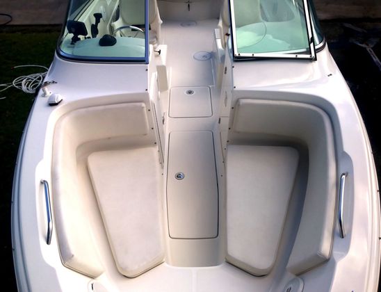 Bow deck of a white powerboat showing bench seating, a central storage hatch and stainless grab rails.