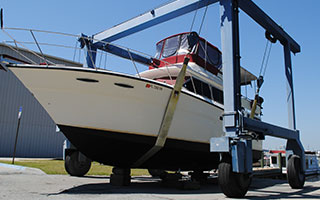 A white motor yacht with a blue hull hoisted on a travel lift in a boatyard.