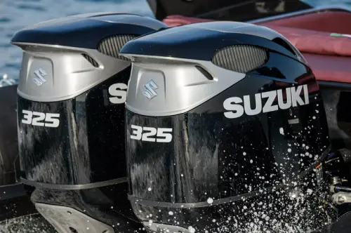 Twin Suzuki 325 outboard motors on the transom of a boat, splashing through water.