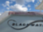 Boat hull with painted Blackwater lettering against a cloudy sky.