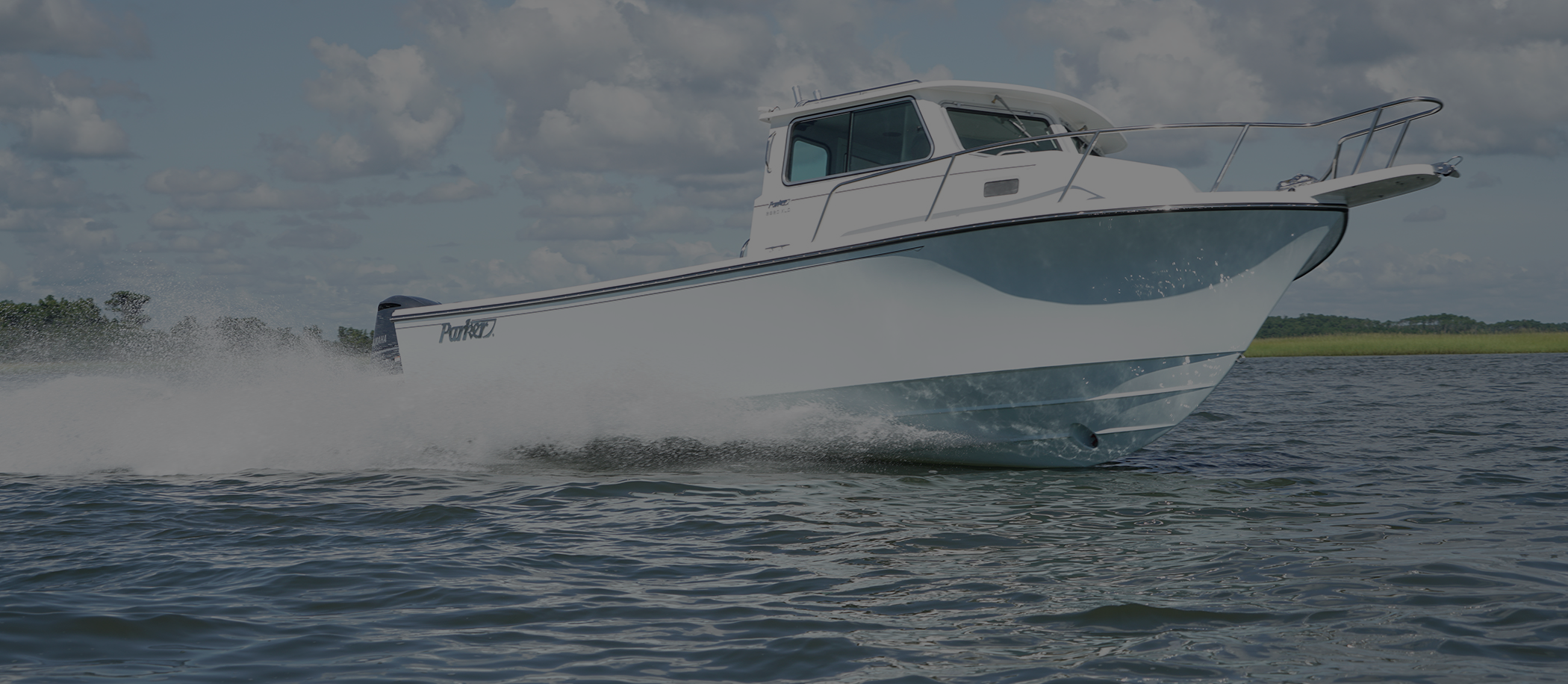 Parker center-console-style cabin boat running at speed on a calm tidal waterway with marsh grass in the background.