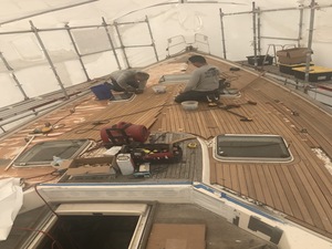 Teak deck of a yacht under a white protective tent with workers removing old planking and fittings.