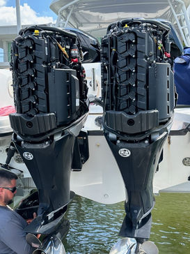 Twin black outboard motors mounted on the back of a white boat, with a person standing at the left edge of the frame.