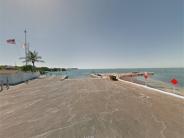 Concrete waterfront dock with a flagpole and palm tree overlooking open water.