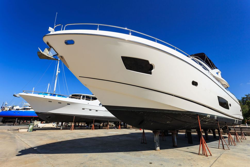 Two white motor yachts raised on stands in a boatyard with blue sky overhead.