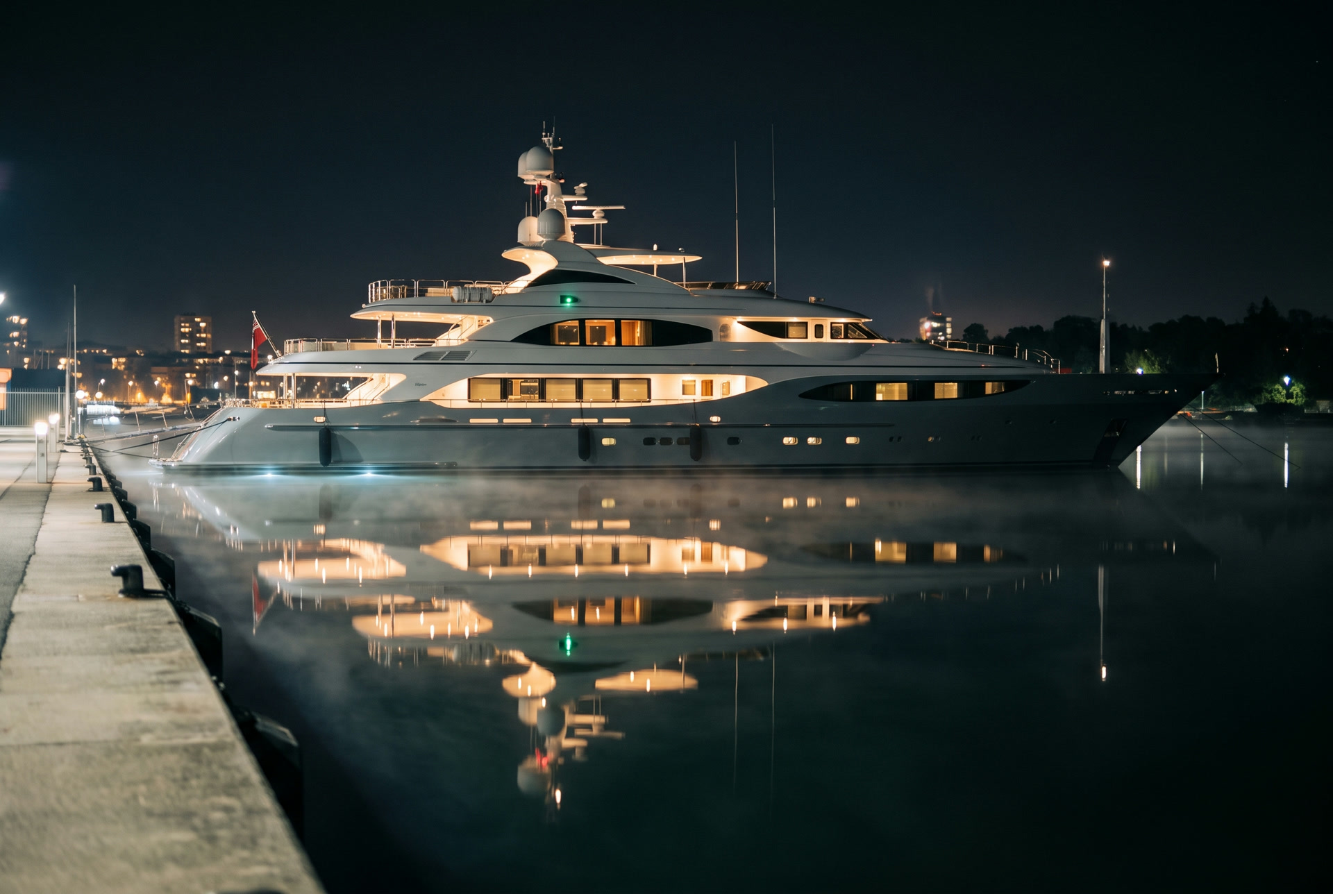 Large white motor yacht moored at a quay at night, its lights reflected on the still water, shown without a identifiable business name or town.