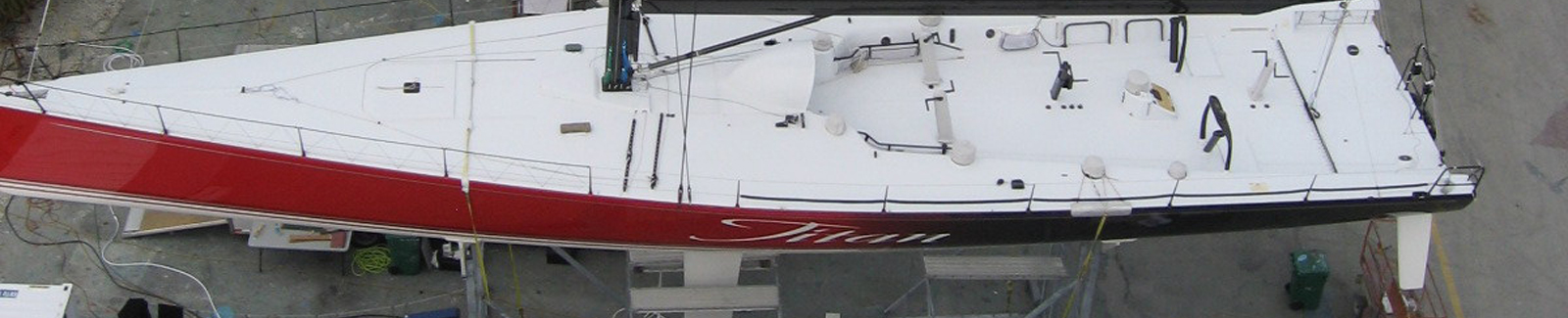 Aerial overhead view of the racing sailboat Titan with a red hull and white deck resting on stands at a boatyard.